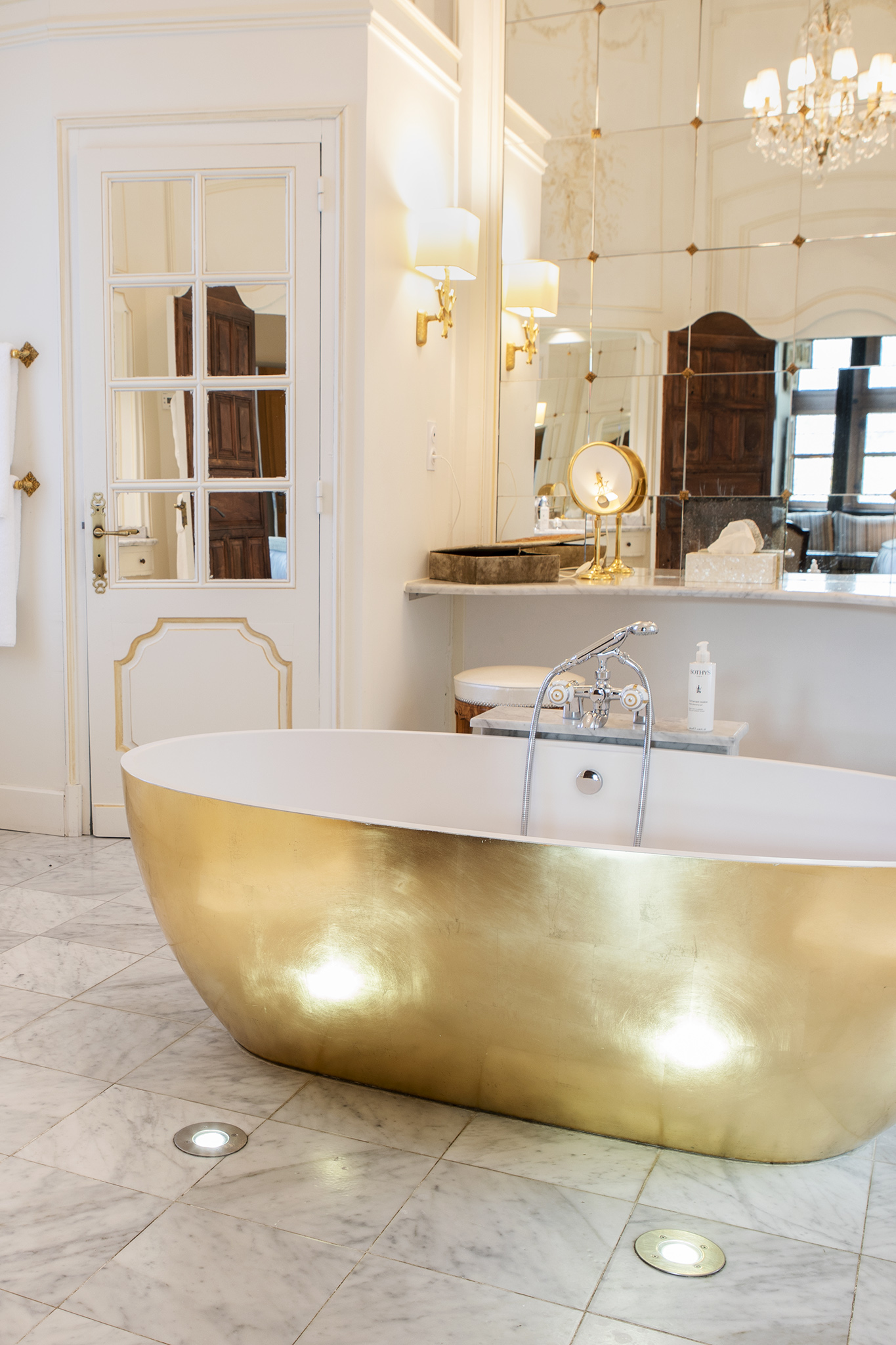 Bild på det stora gyllene badrummet i Château de la Treyne, där ett badkar i guld är placerat mitt i rummet och väggarna kläds av stora speglar.